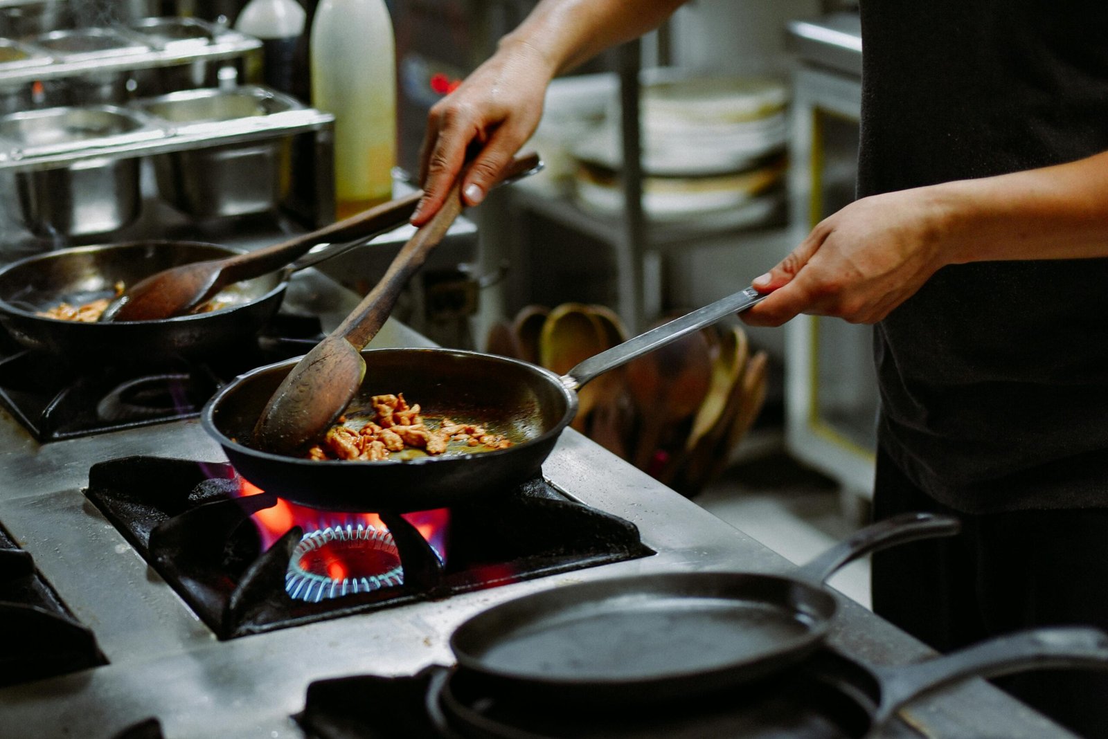 Chef preparing a dish with sautéed ingredients in a restaurant kitchen.