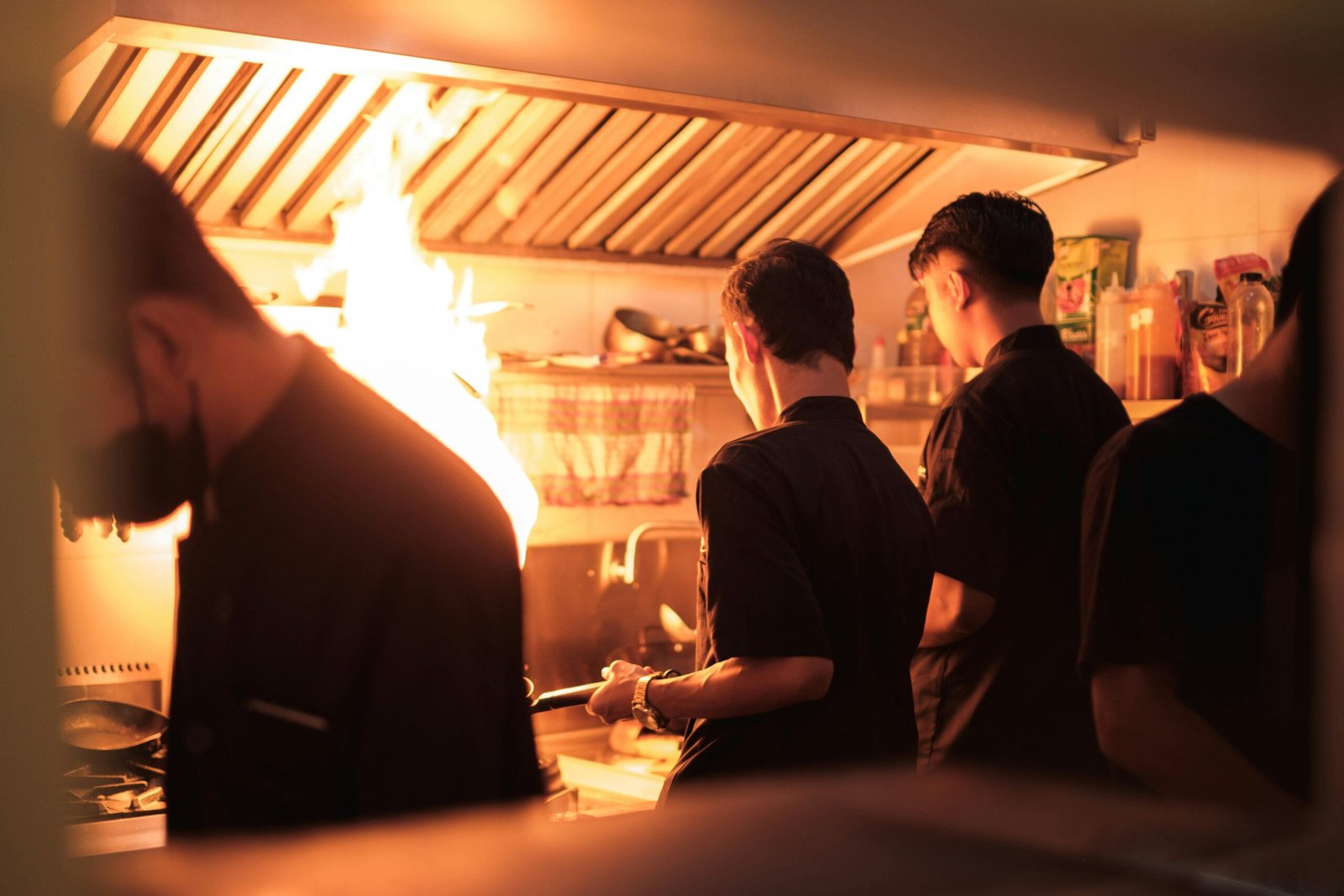 Professional chefs working in a busy industrial kitchen with visible flames.